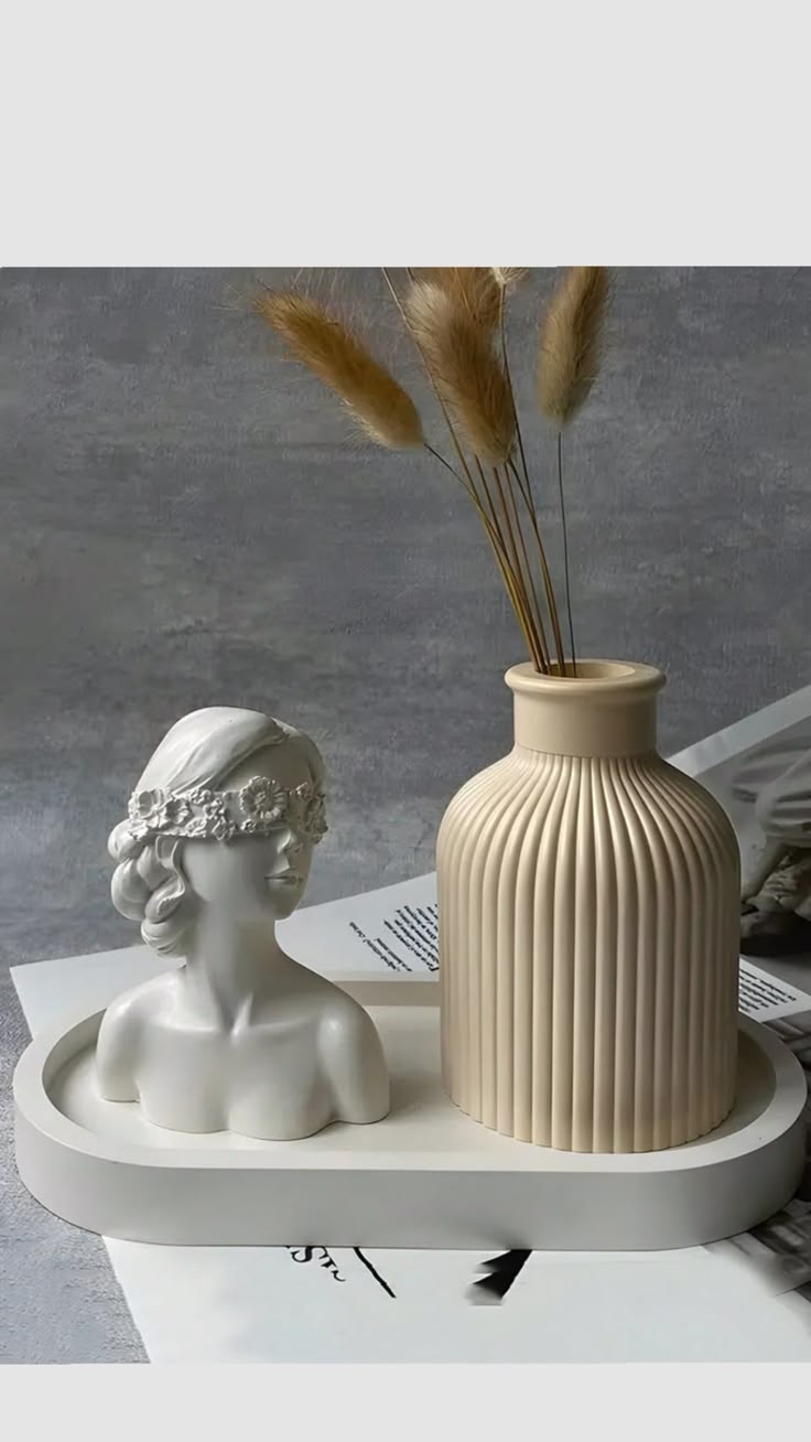 Classical sculpted maiden bust with floral crown beside fluted cream bottle vase on tray