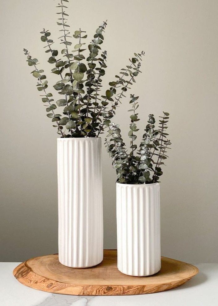 Pair of tall fluted cylindrical vases with eucalyptus foliage on wood platter