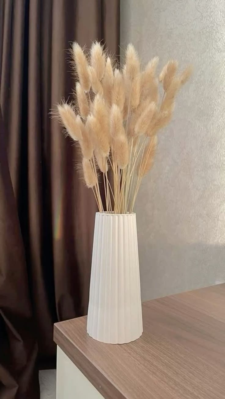 Ribbed white tapered vase with fluffy dried bunny tails on wooden credenza